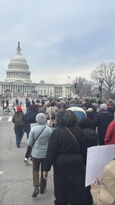 A large group of people carrying signs and walking towards the Capitol on a cold winter day.