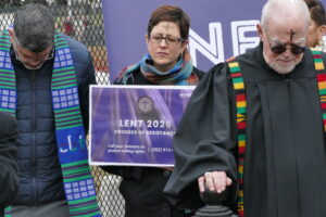 Laurie stands with two other faith leaders praying with their eyes closed.
