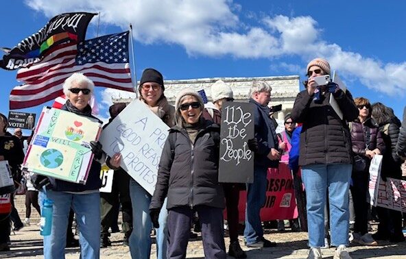Friends stand on the steps of the Lincoln Memorial with signs and smiles