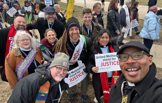 Diverse group of faith leaders holding protest signs and in "selfie" style at a protest.